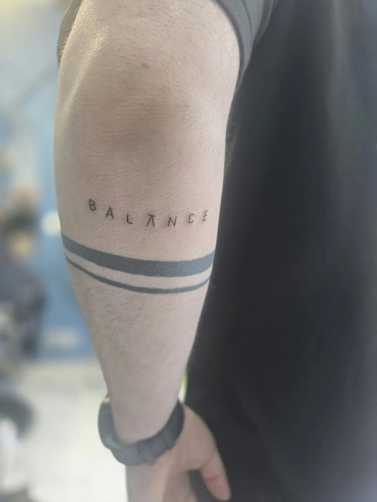 Het woord BALANCE met een pi-teken als A, boven twee zwarte armbanden op de arm