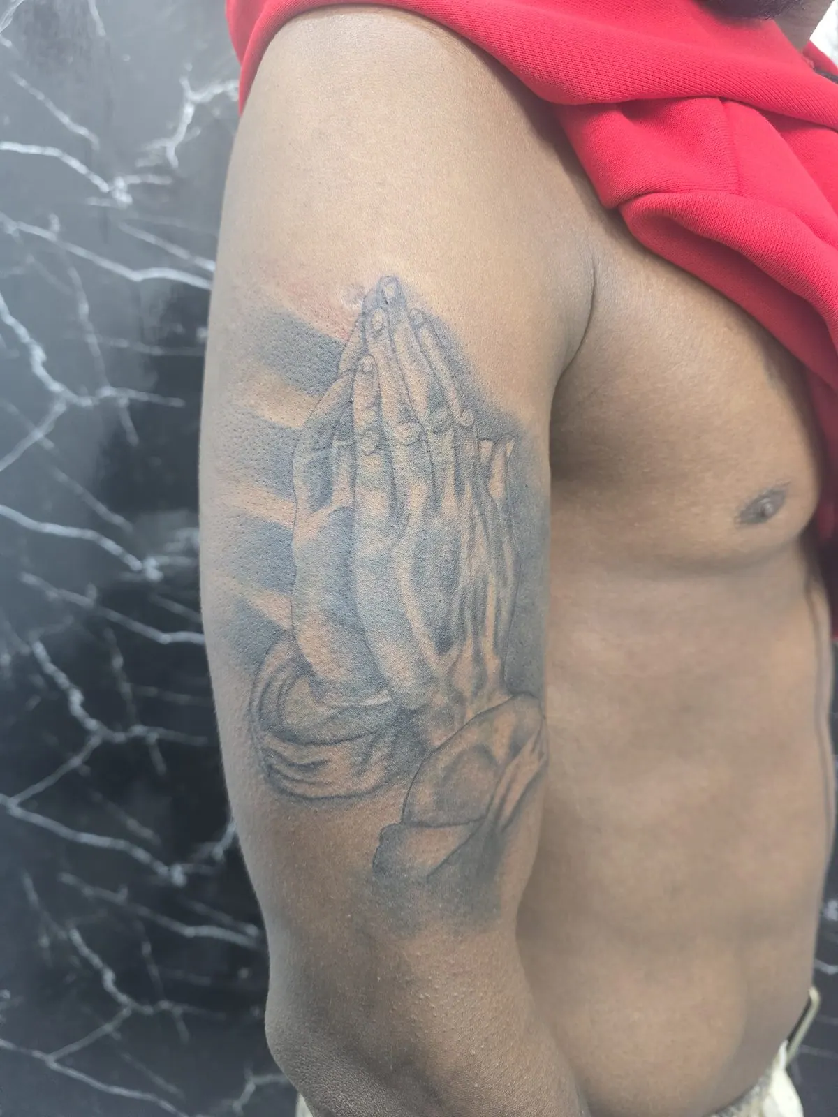 Realistische zwart-grijze tattoo van biddende handen op de bovenarm