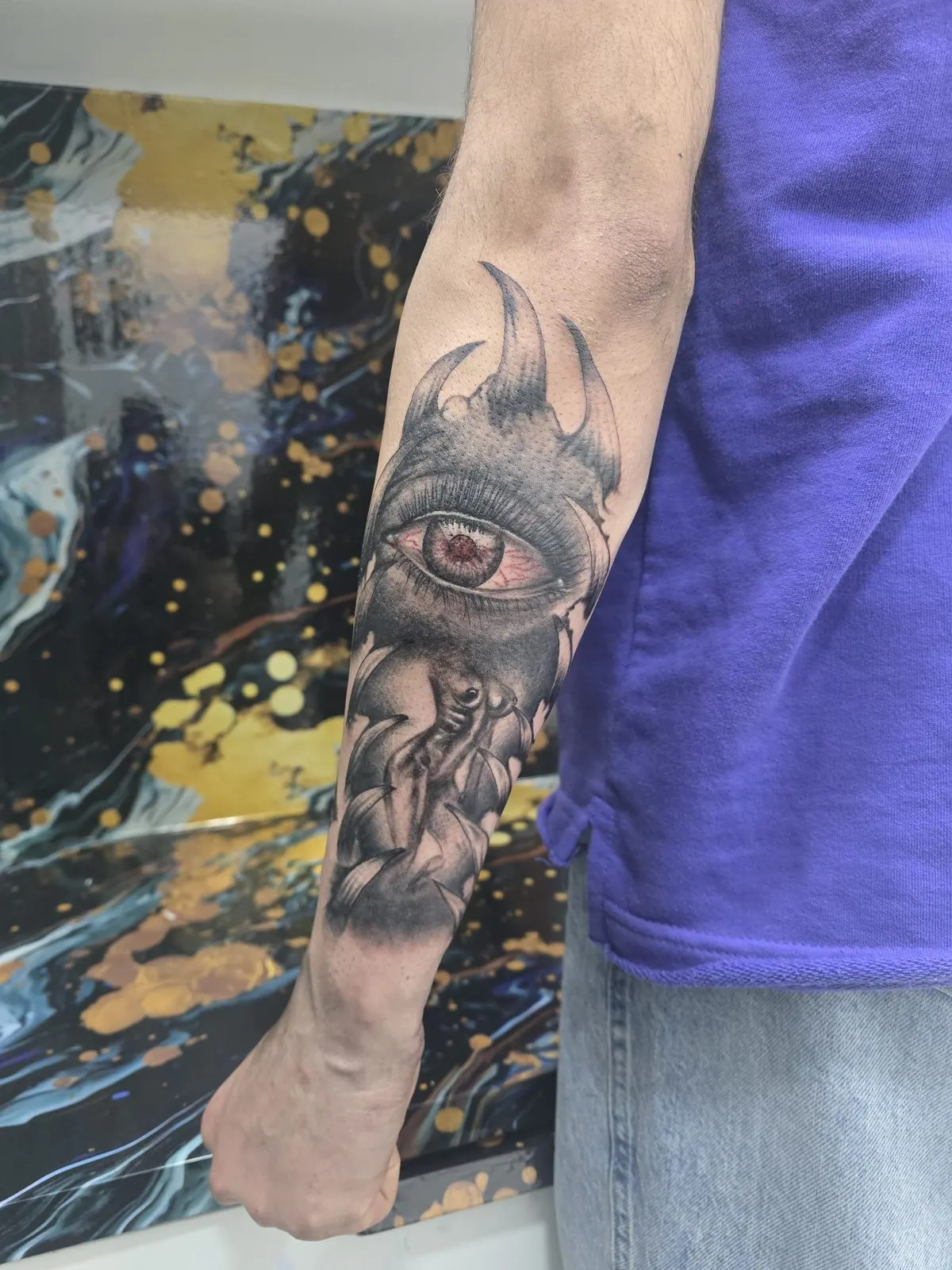 Zwart-grijze tattoo van een realistisch oog met een rode iris op de onderarm